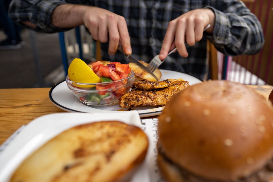 אדם חותך מנת חזה עוף שלצידו מוגש סלט במסעדה ב"שוק תלפיות" בחיפה